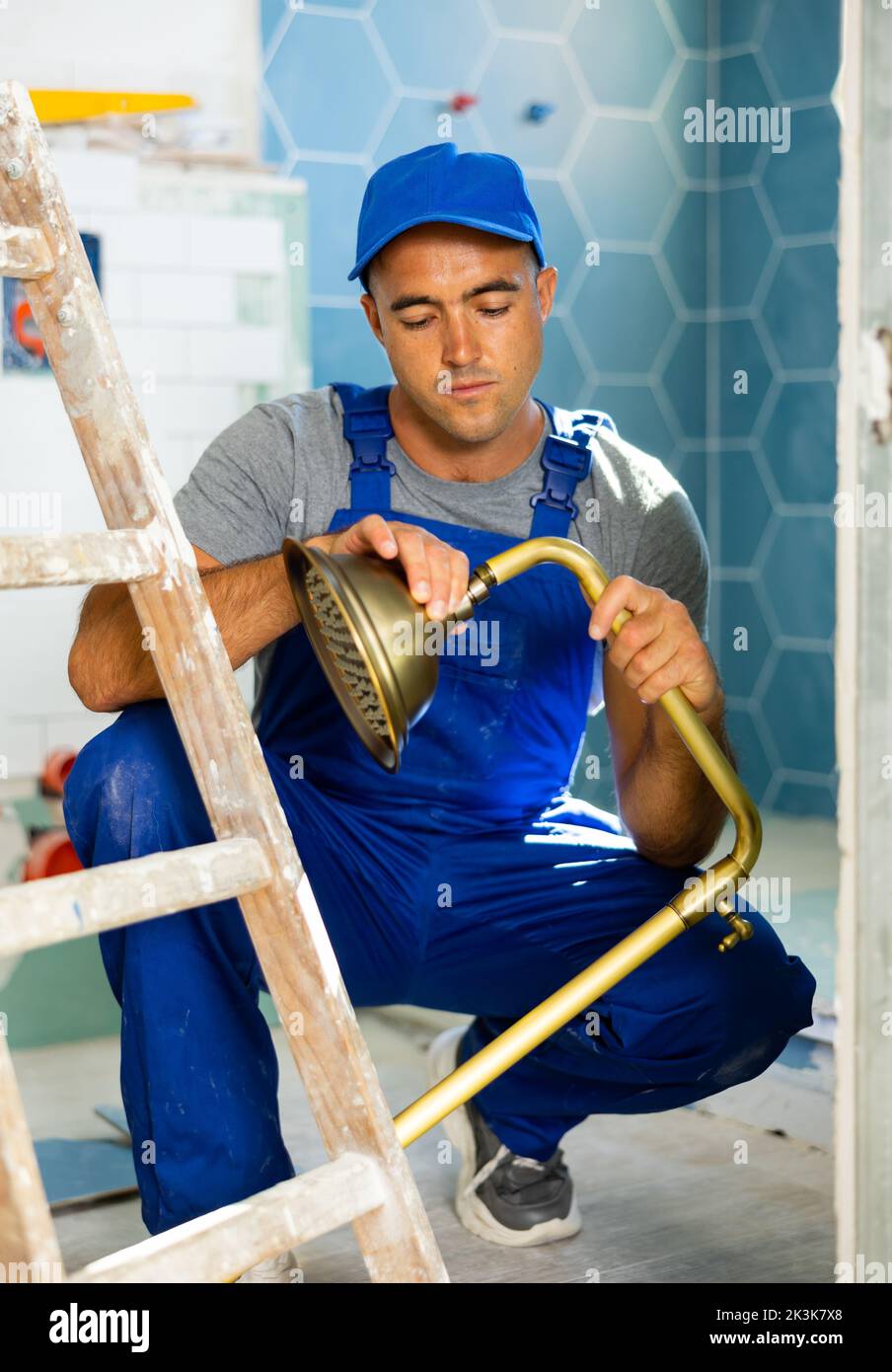 Skilled workman wearing in blue construction overalls sitting squat and
