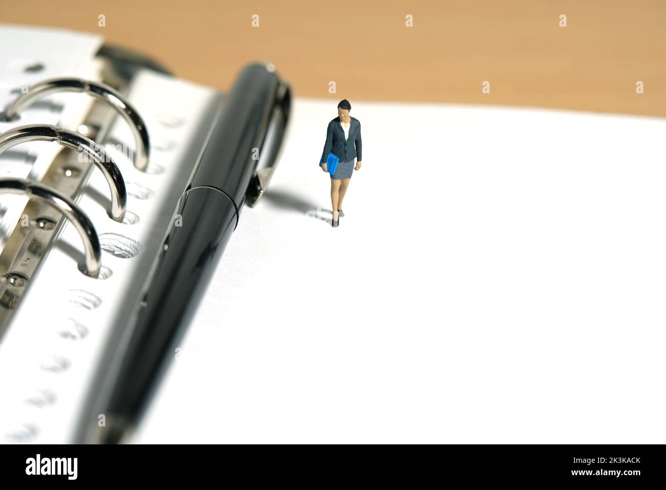 Miniature people toy figure photography. Minutes of meeting, schedule, task checklist concept. A businesswoman standing walking above notebook with pe Stock Photo