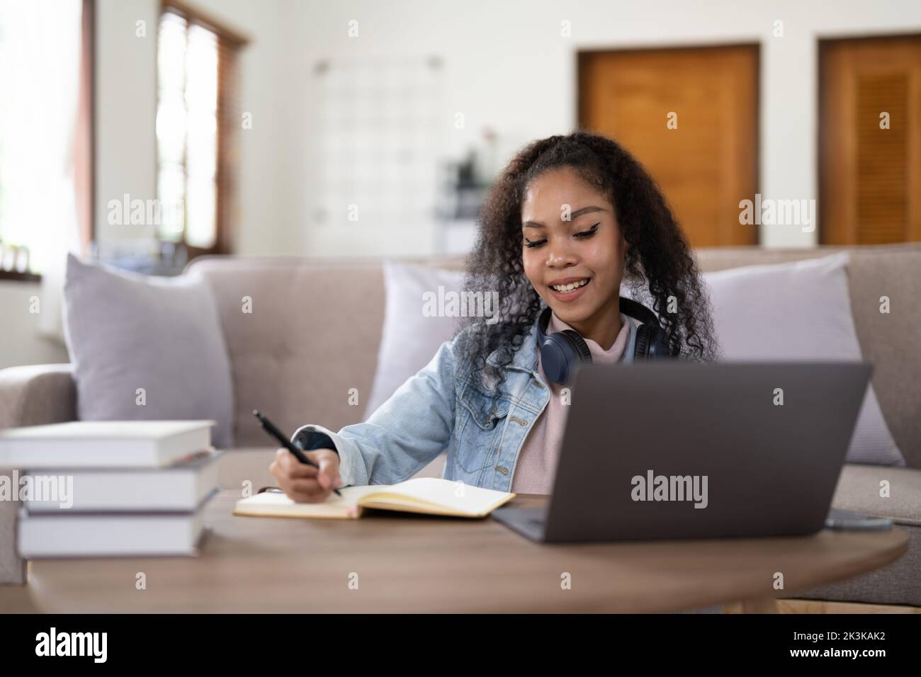 Student woman in headphones writing notes in notebook watching webinar video course, female student looking at laptop listening lecture study online Stock Photo