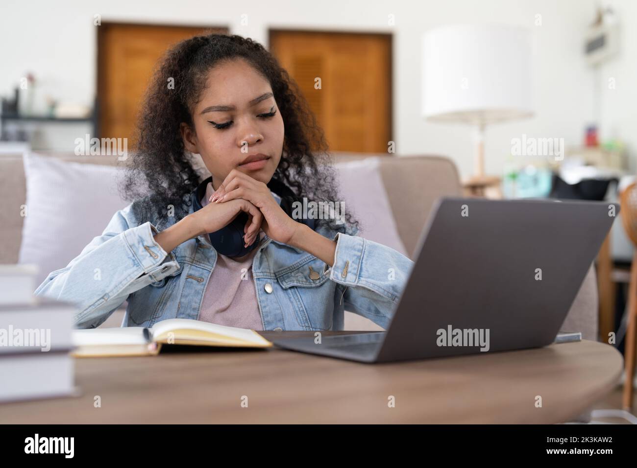 Student woman in thinking writing notes in notebook watching webinar video course, female student looking at laptop listening lecture study online on Stock Photo