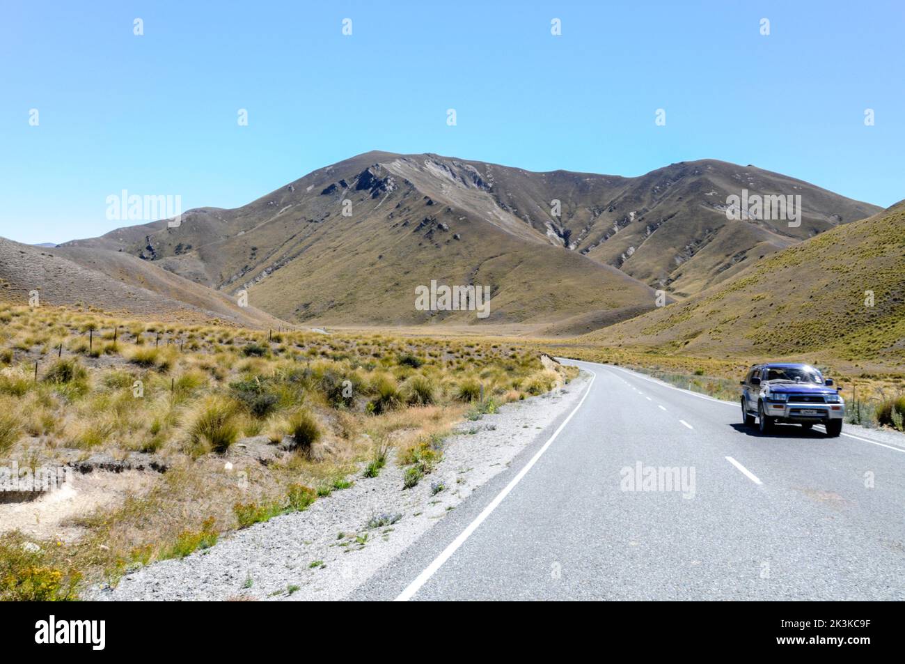 Lindis Pass, a mountainous road (Highway 8) across a barren landscape of tussock grasslands in the Lindis Pass Scenic Reserve in the ecoregion of Sout Stock Photo