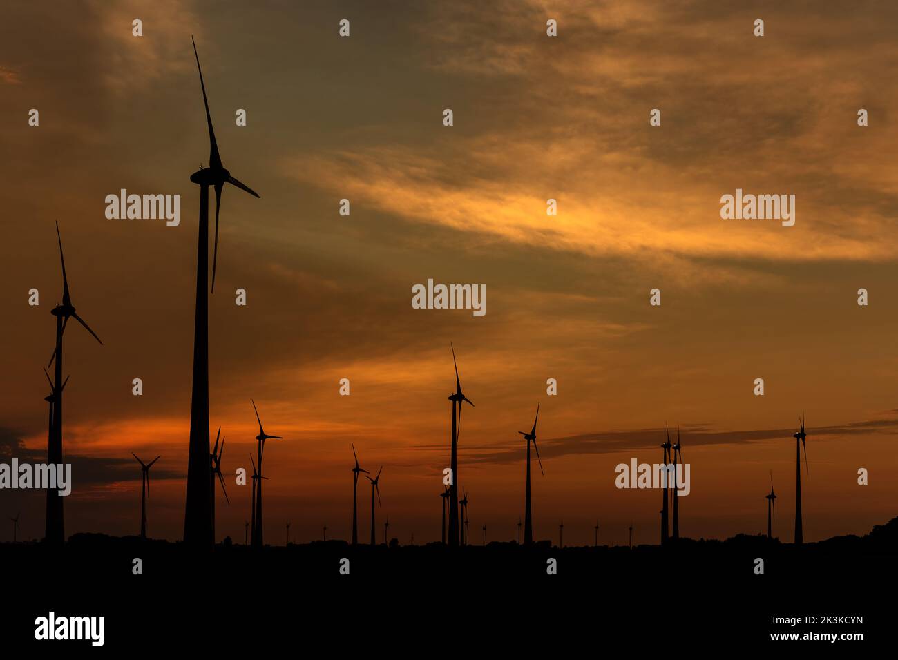 Silhouettes of wind turbines producing renewable energy at sunset Stock Photo