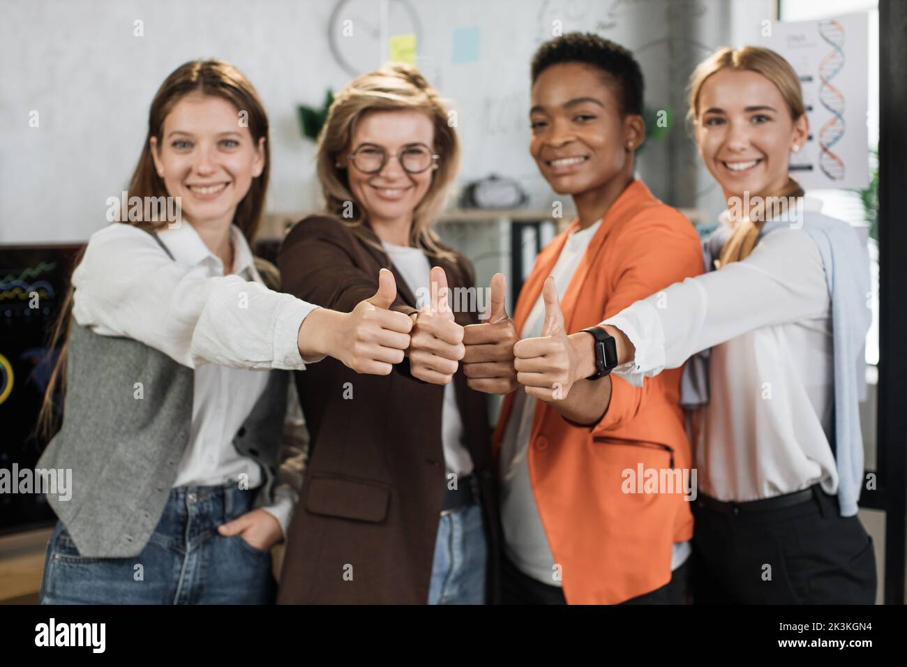 Four multi ethnic female office workers showing thumb up and smiling on