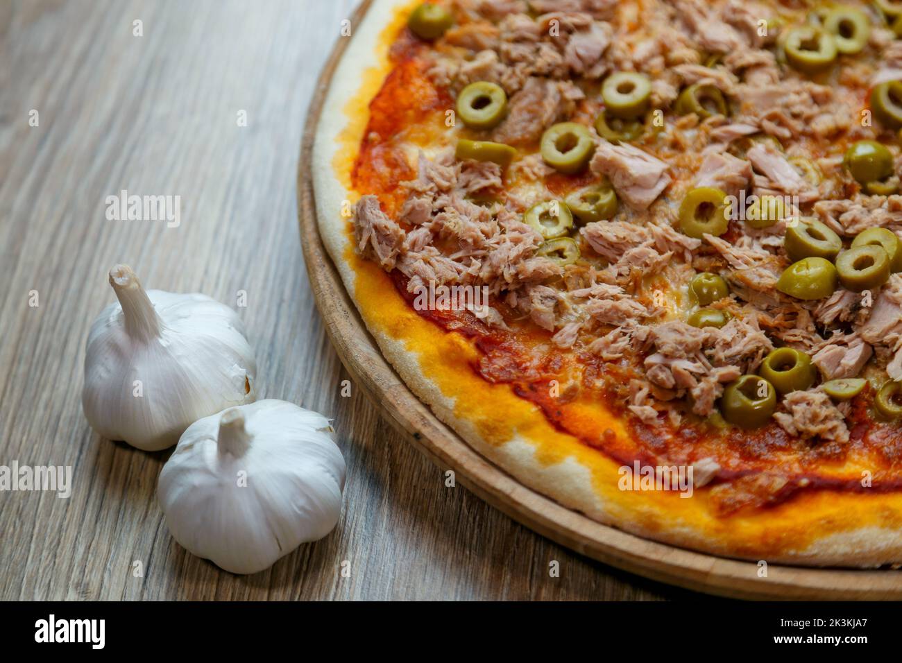 A closeup shot of crusty Italian pizza with meat, green olives, and garlic on the wooden table Stock Photo