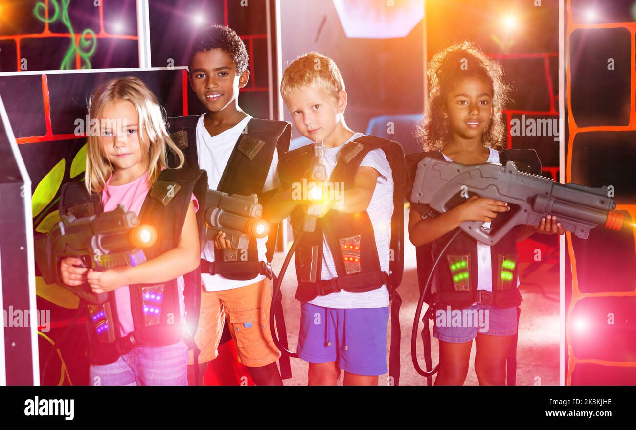 Joyful teens aiming laser guns at other players during lasertag game in dark room Stock Photo