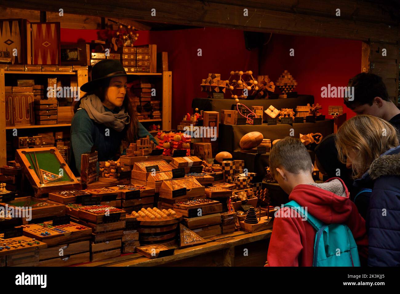 The market trader watches as a mother and her two sons browse an assortment of wooden board games and puzzles on her stall at York Christmas Market. Stock Photo