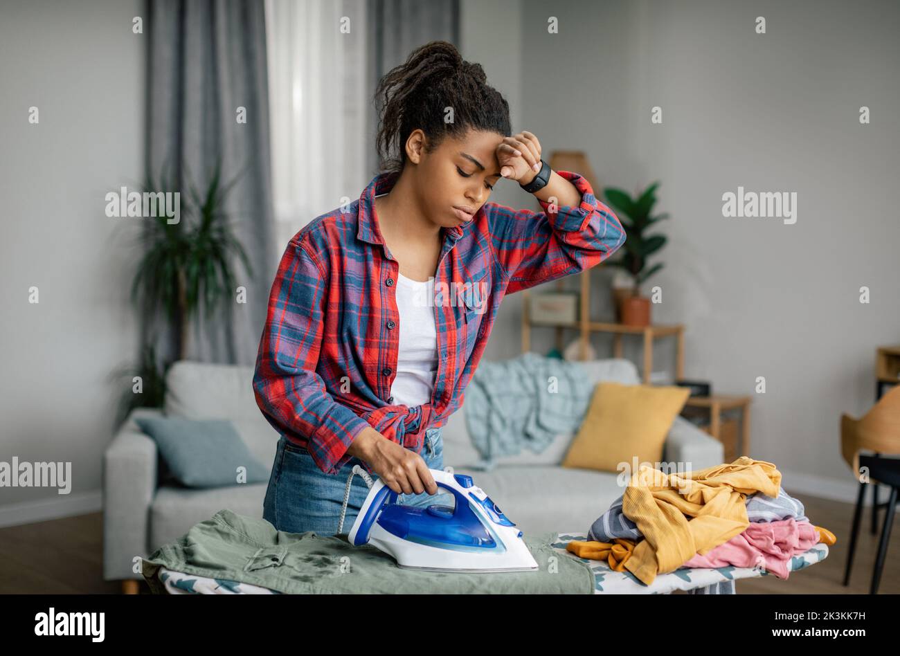 Sad tired pretty young black lady wipes sweat from forehead and irons