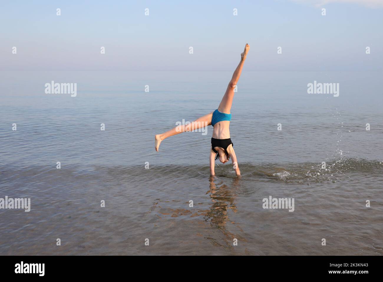 young girl performs gymnastic exercises with her head upside down on