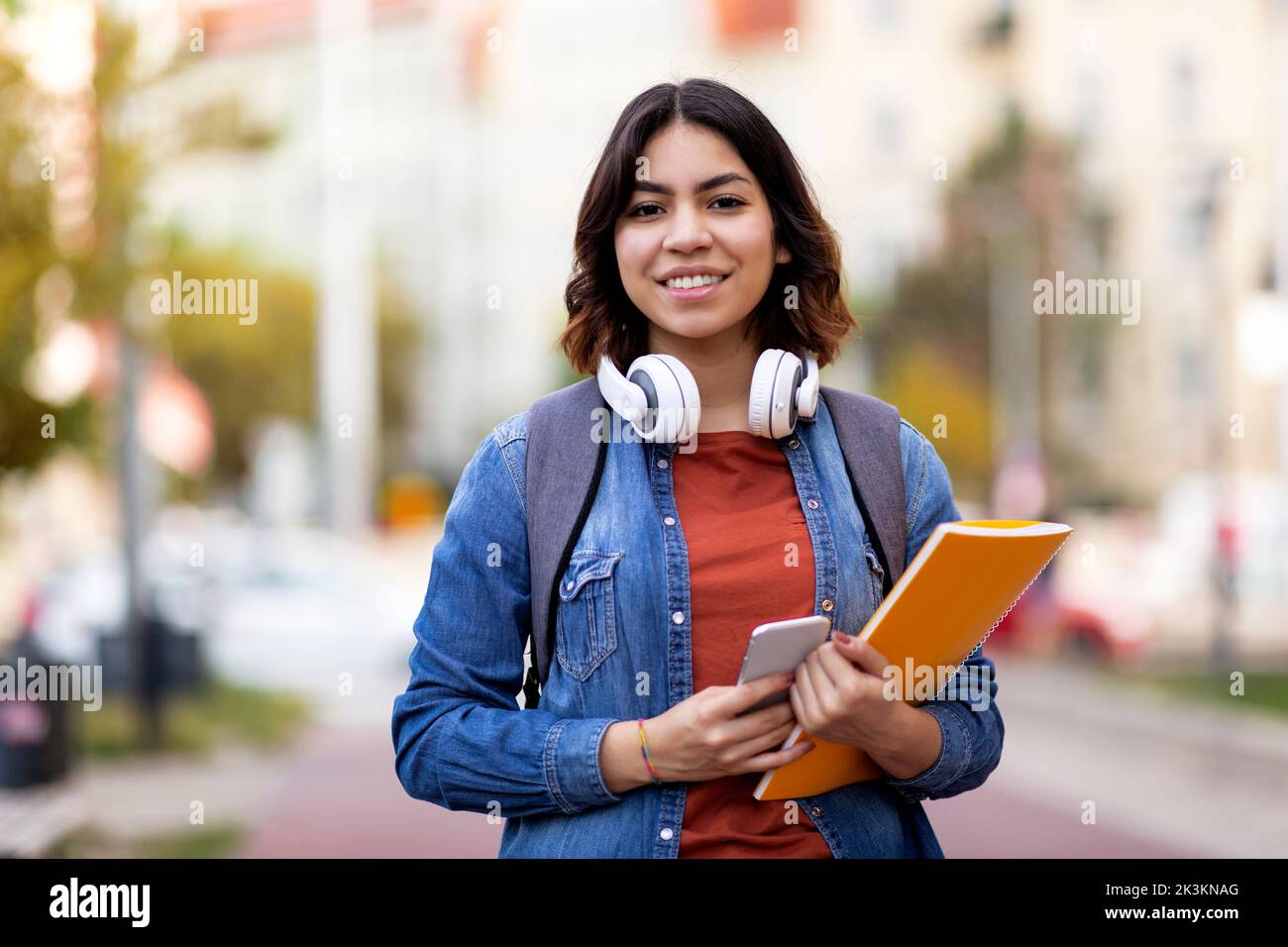 Modern Student. Smiling Young Arab Female With Workbooks And Smartphone Posing Outdoors Stock Photo