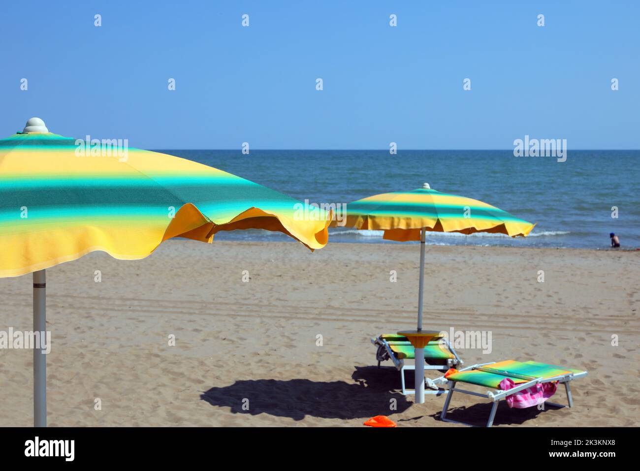 green and yellow colored sun umbrellas on the sandy beach by the sea in summer Stock Photo