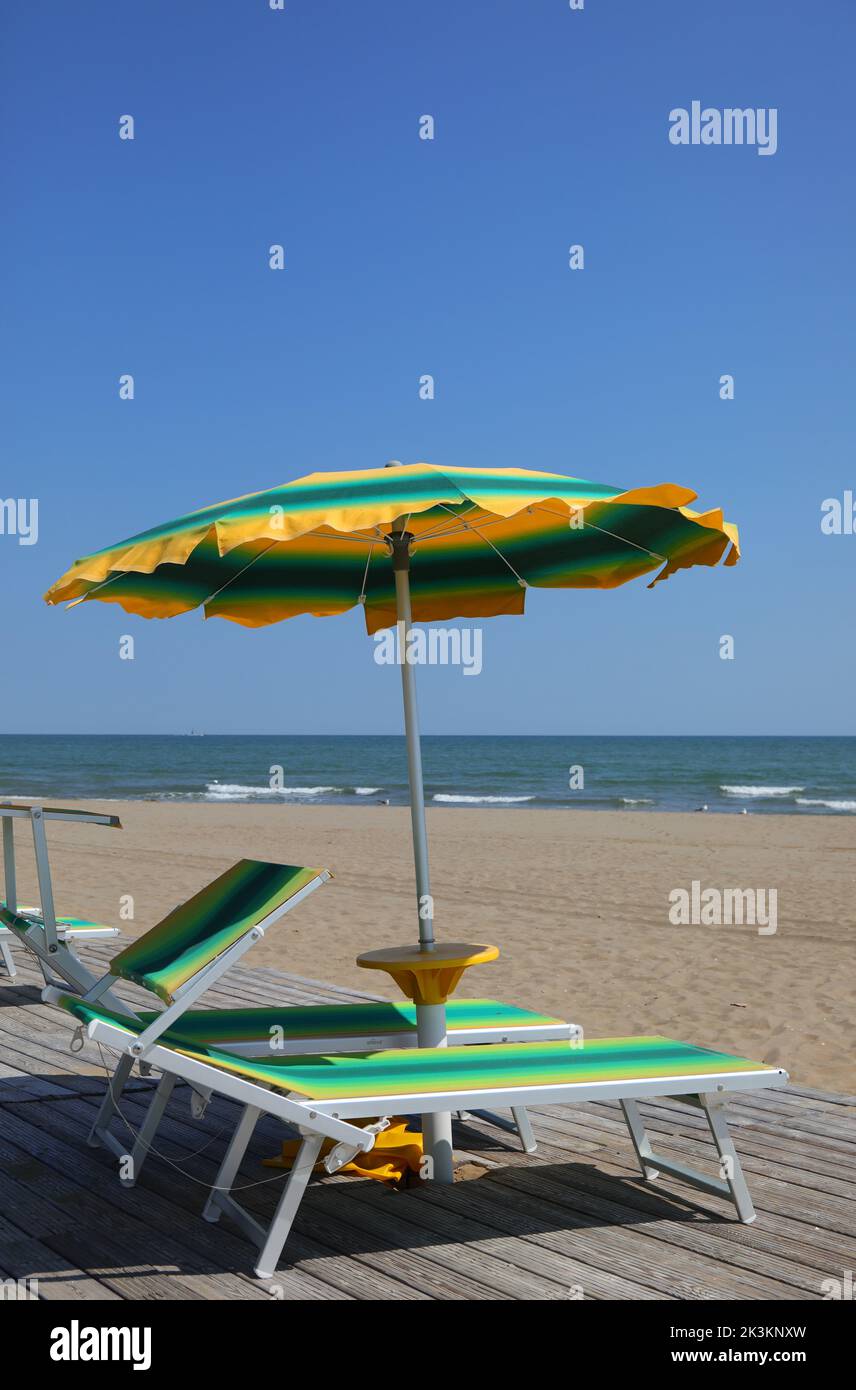 green and yellow colored sun umbrellas on the sandy beach by the sea in summer Stock Photo