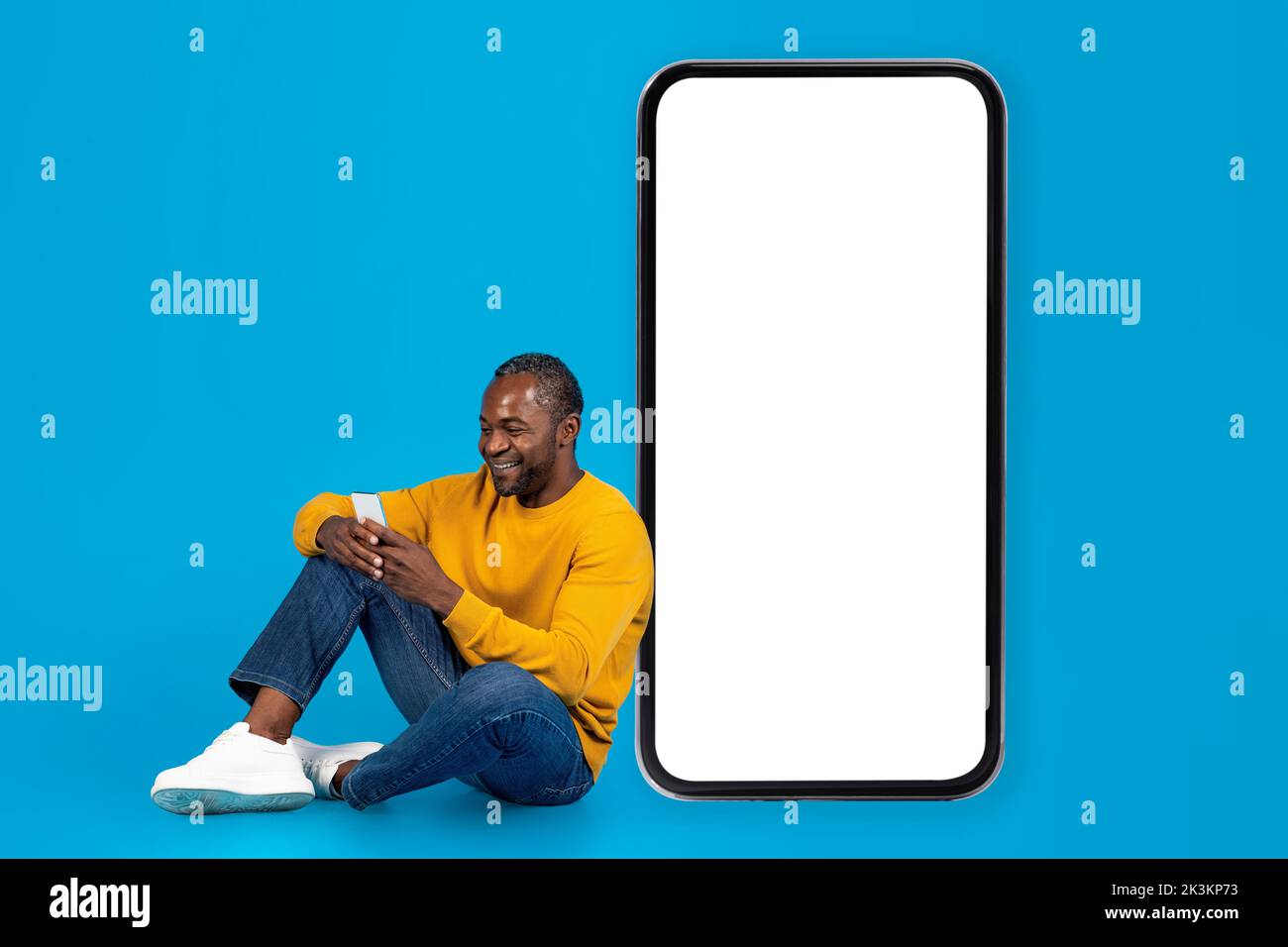 Happy black man sitting on floor, using smartphone Stock Photo
