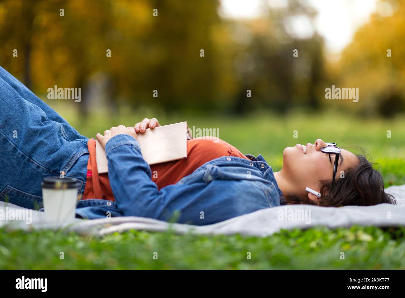 Outdoor Leisure. Nerdy Arab Female In Eyeglasses Lying On Lawn With Book Stock Photo