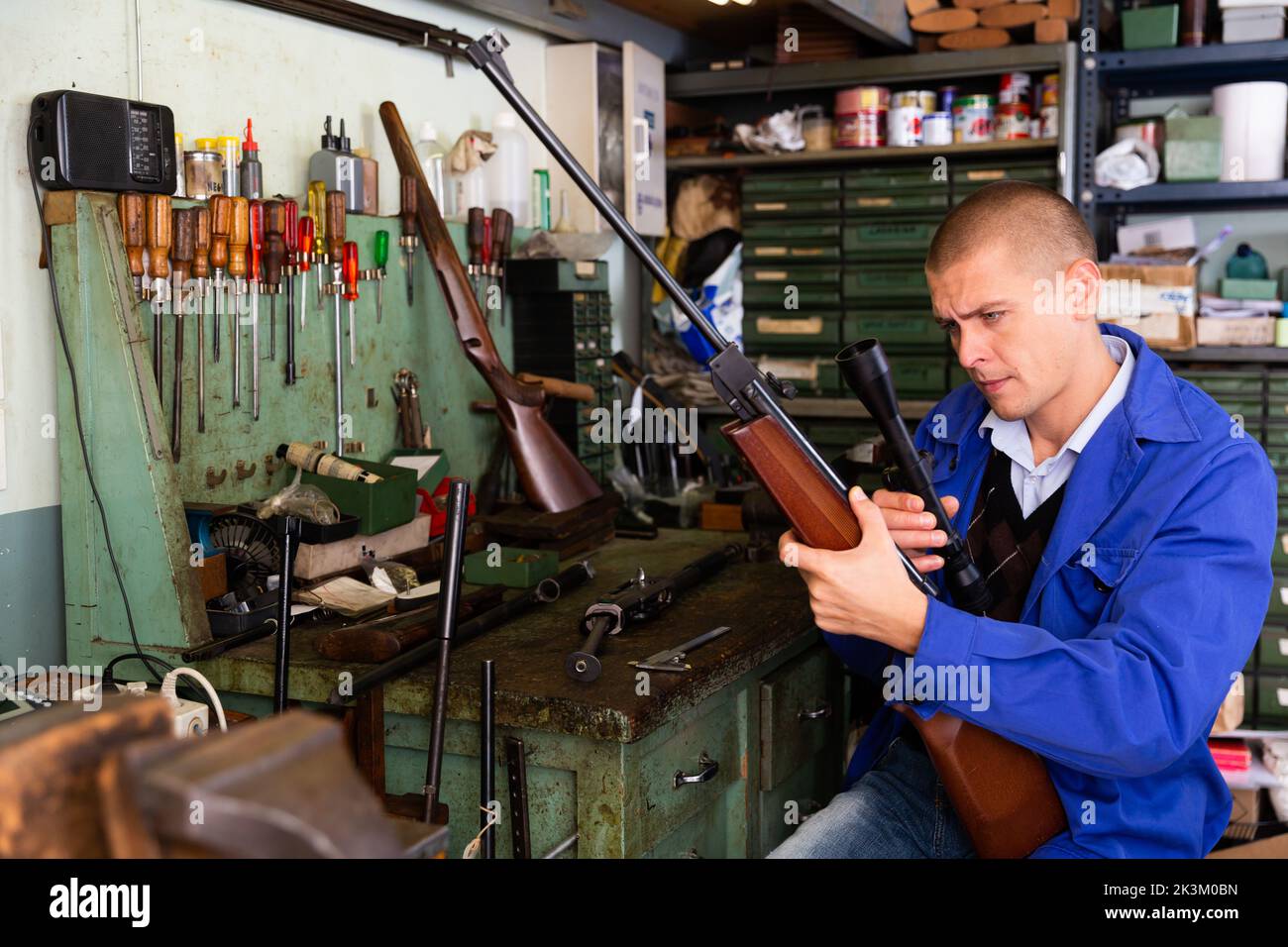 Gunsmith attaches a telescopic sight to rifle in weapons workshop Stock Photo
