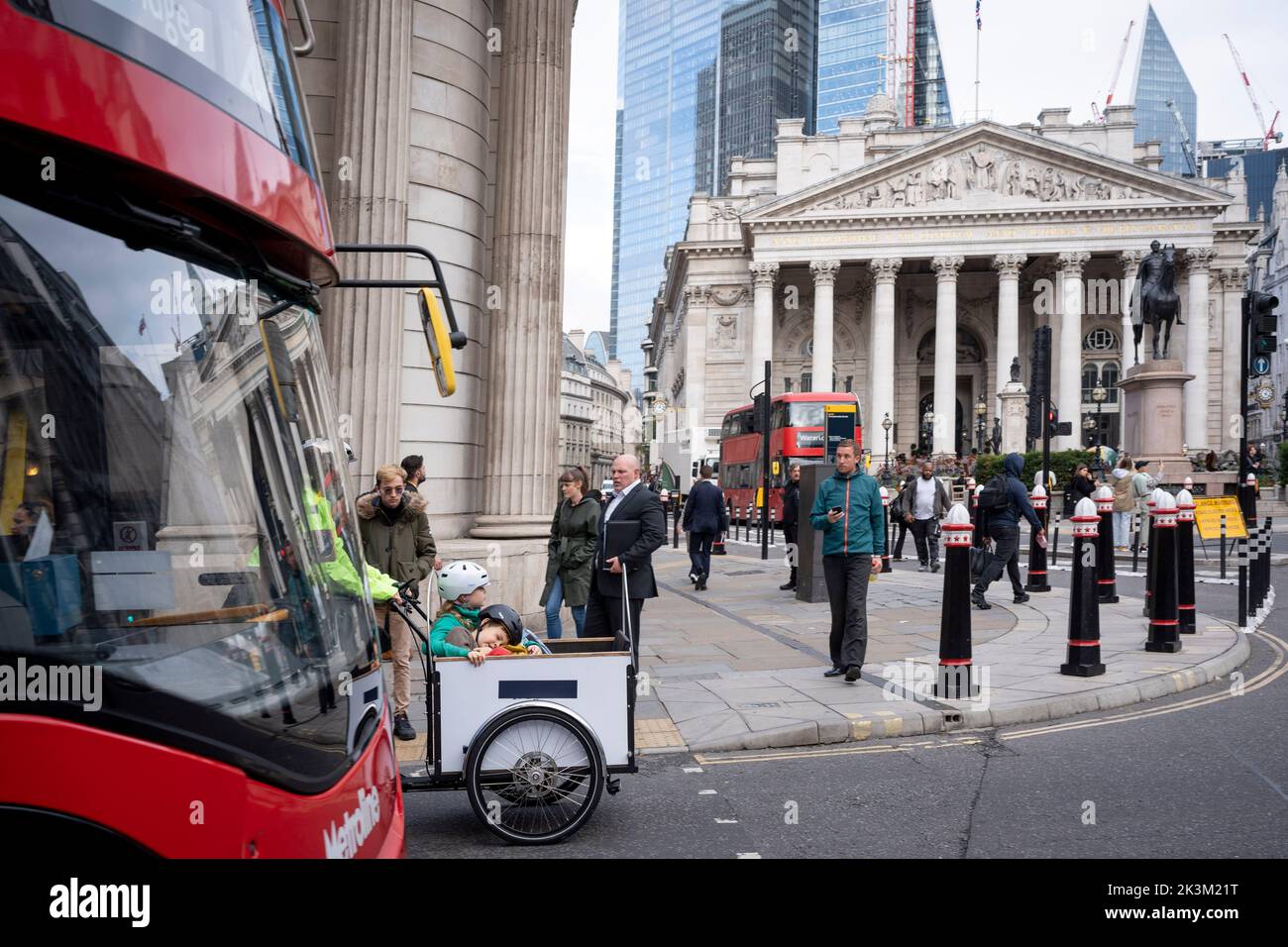 A bus overtakes a woman and two children being carried in the bucket of a cargo bike, past the Bank of England at the junction of Princes and Threadneedle Streets EC2 in the City of London, on 26th September 2022, in London, England. Stock Photo