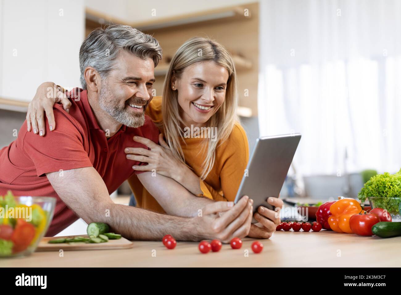 Happy spouses using digital tablet while cooking Stock Photo