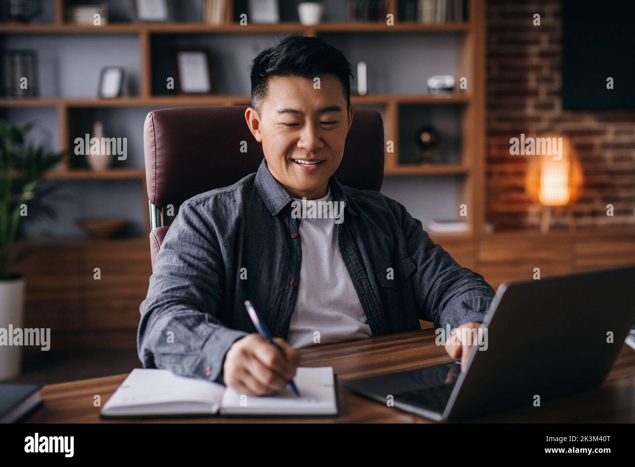 Cheerful mature korean male working at table with laptop, businessman analyzing data stock in home office Stock Photo
