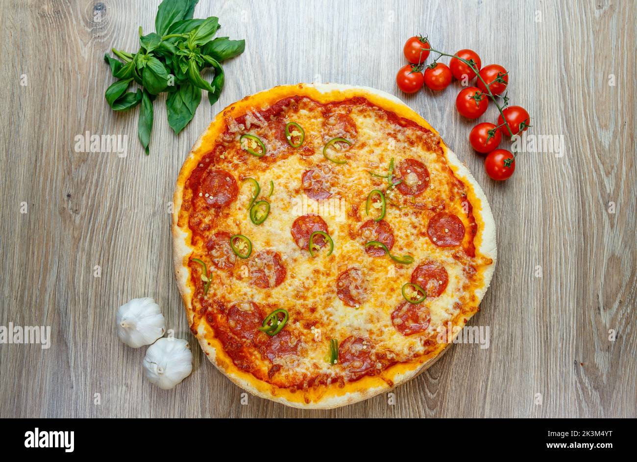 A top view of Pizza Diavola with salami, mozzarella, green hot pepper with ingredients next to it on a wooden table Stock Photo