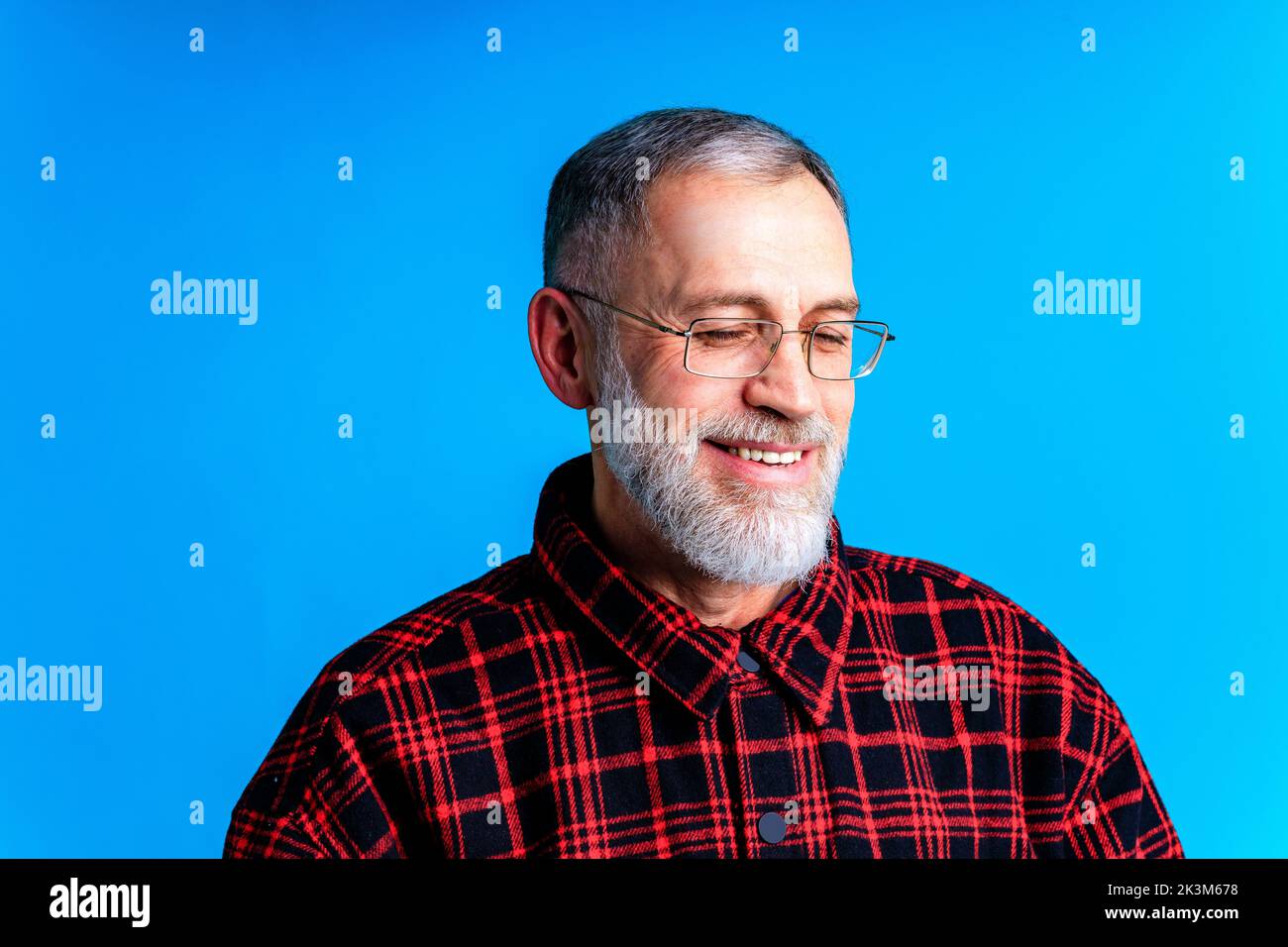 Close-up portrait of intelligent shy man looking down in blue studio background Stock Photo