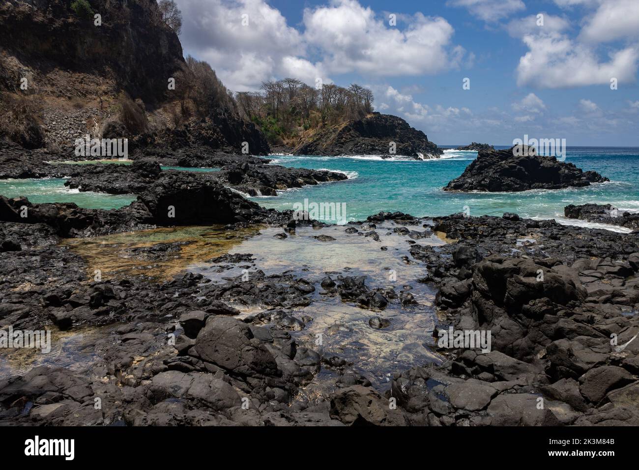 Black rocks on the wet Baia dos Porcos beach on Fernando de Noronha ...