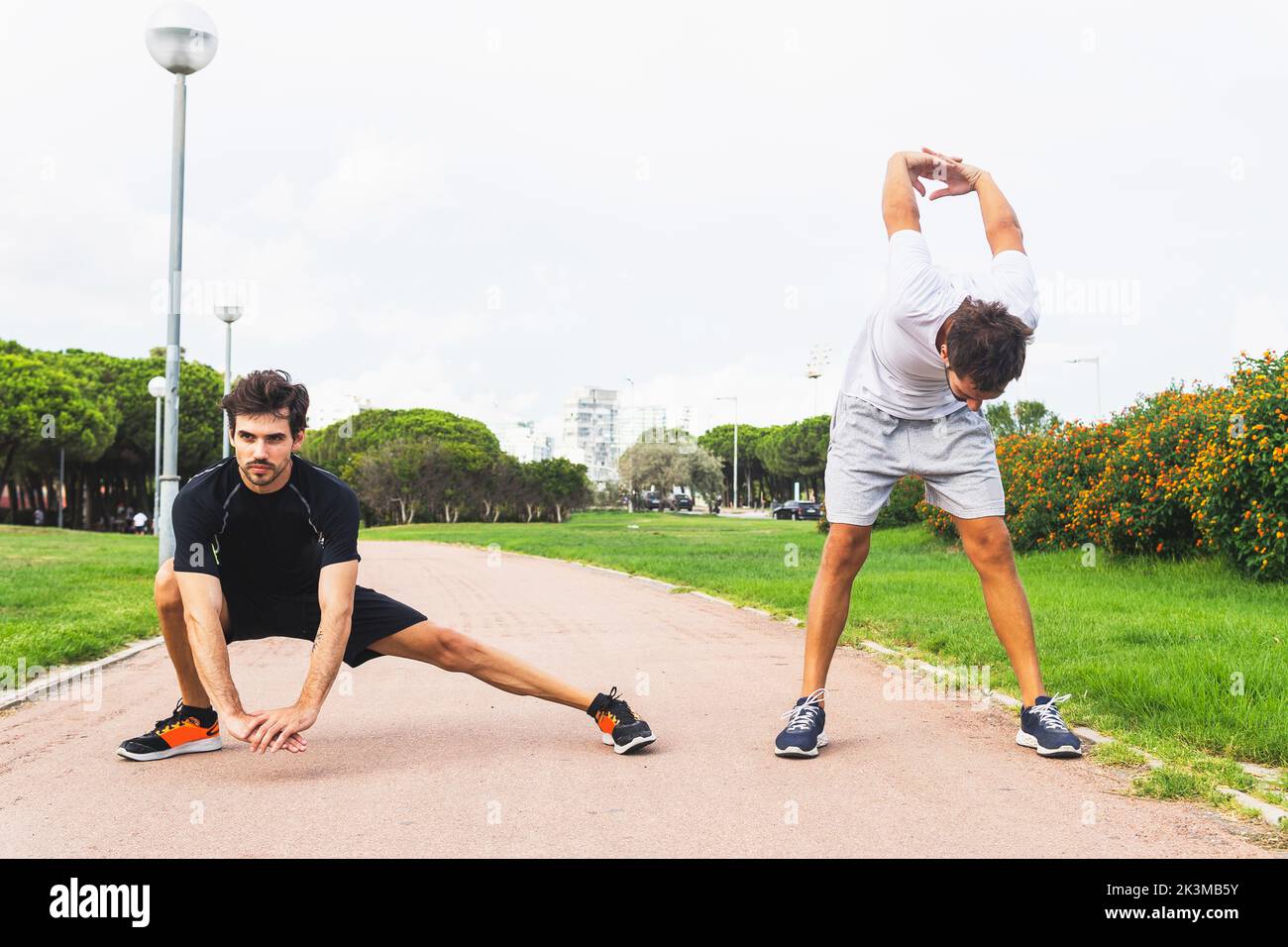 Full body Hispanic male athlete lunging and bending forward with hands behind back while stretching on path during fitness workout in park Stock Photo