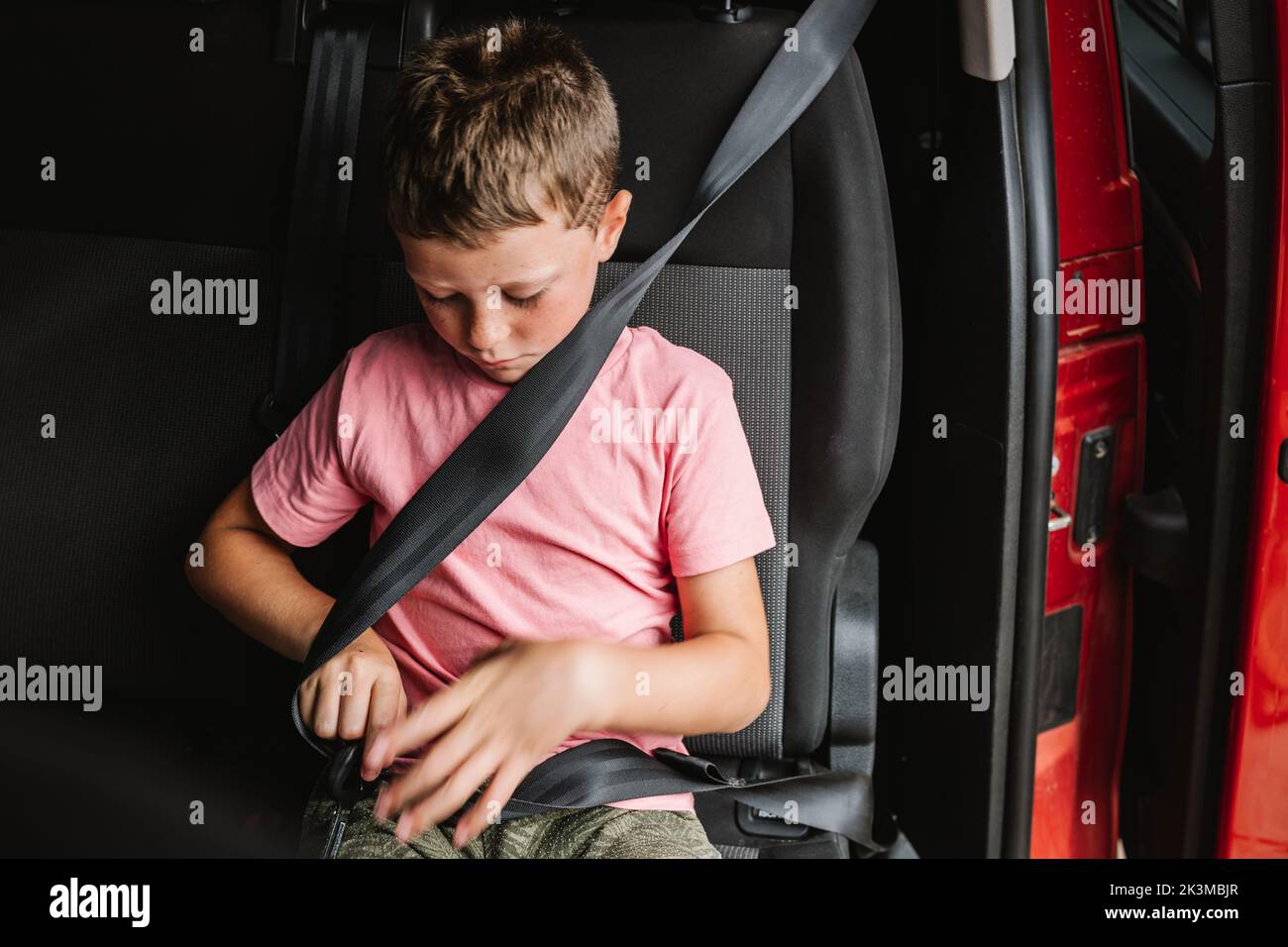 Unemotional boy in casual clothes buckling up while sitting on seat