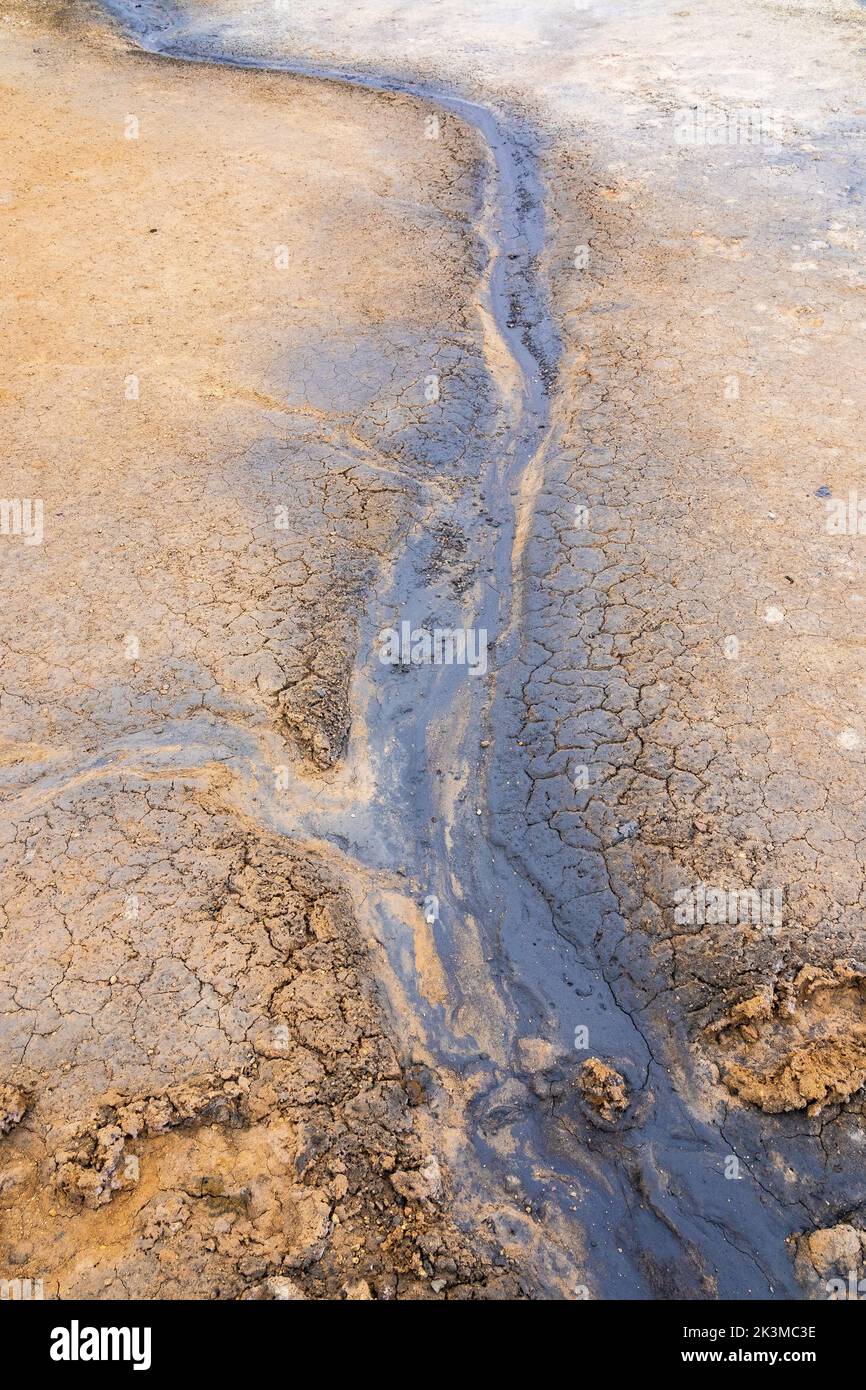 From above thin stream of dirty water flowing on uneven muddy ground on winter day in Hverir geothermal area in Reykjahlid, Iceland Stock Photo