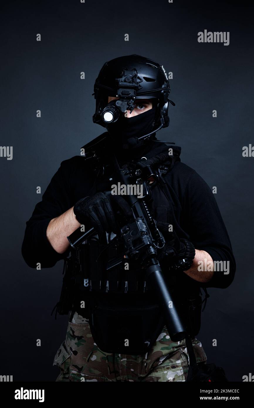 Unrecognizable concentrated male squad fighter in black protective gear and helmet in dark room Stock Photo