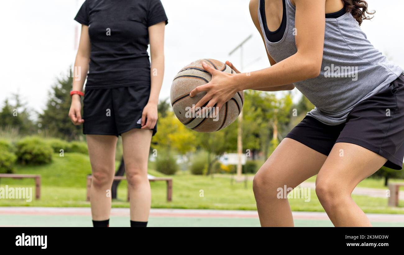 Cropped unrecognizable female athlete blocking opponent dribbling ball during basketball match on cloudy summer day in park Stock Photo