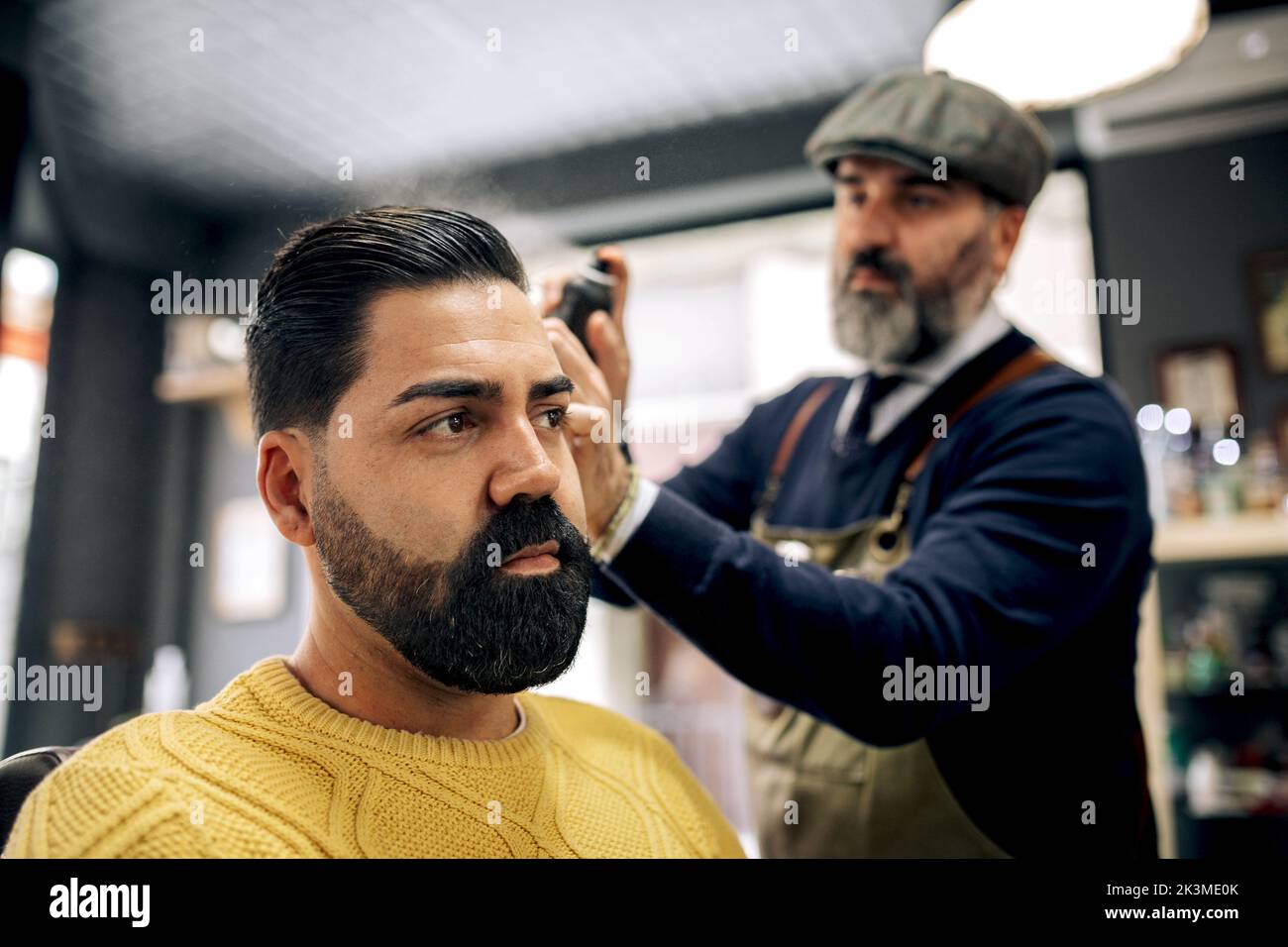 Concentrated middle aged bearded ethnic male barber in apron and beret