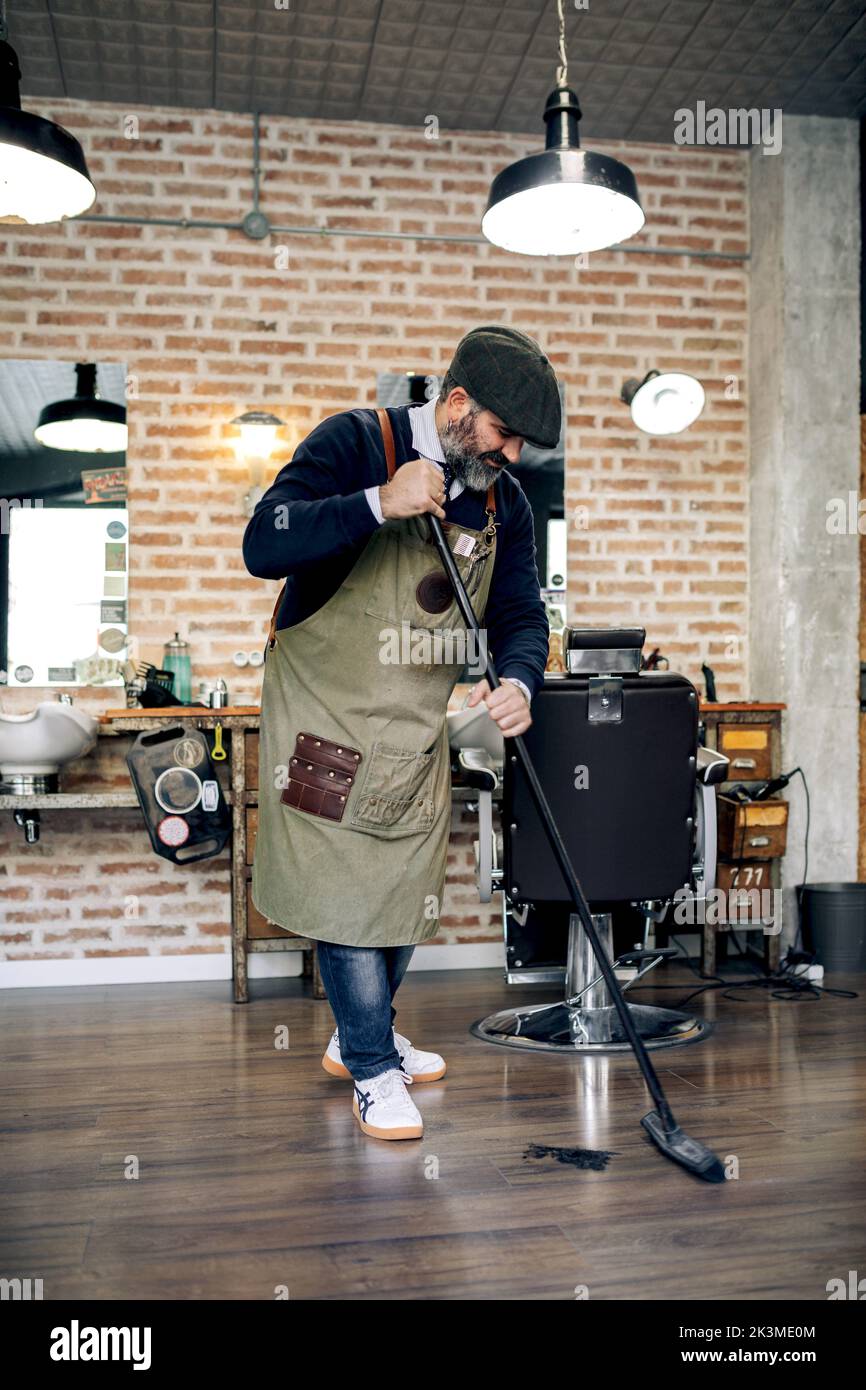 Full length of middle aged bearded Hispanic male barber in apron and