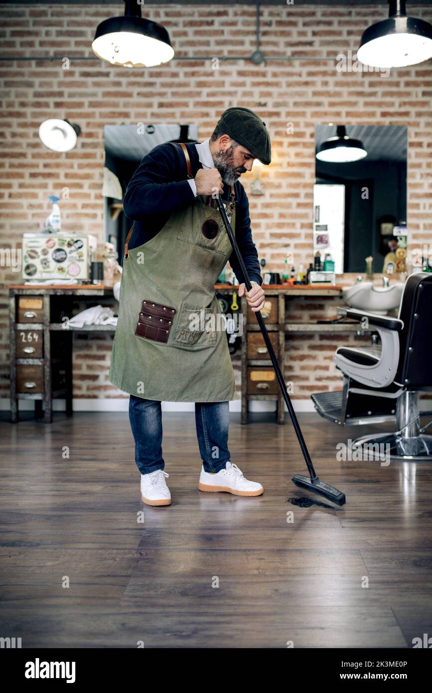 Full length of middle aged bearded Hispanic male barber in apron and