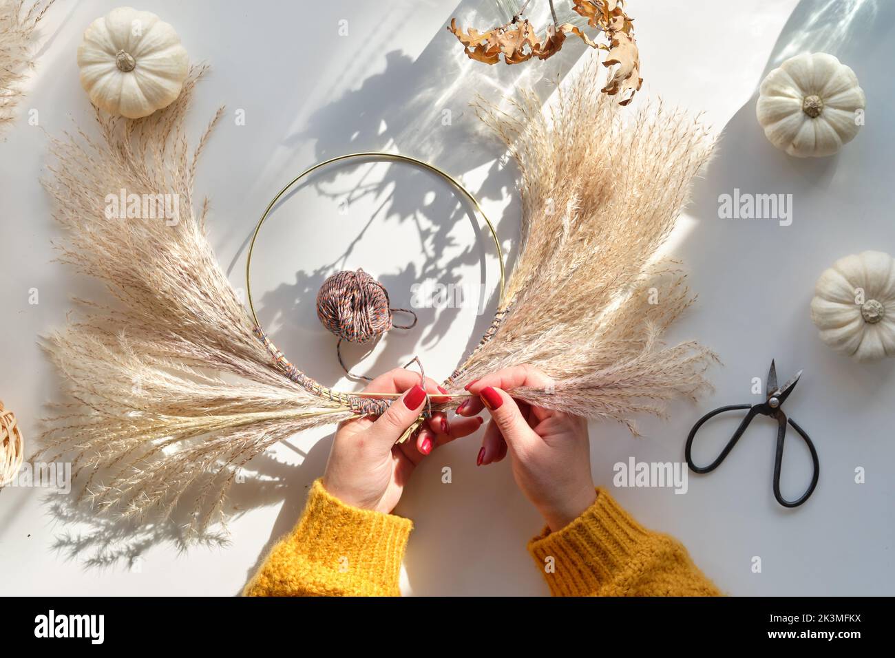 Hands making dried floral wreath from dry pampas grass and Autumn leaves. Hands in sweater tie decorations to metal frame. Stock Photo