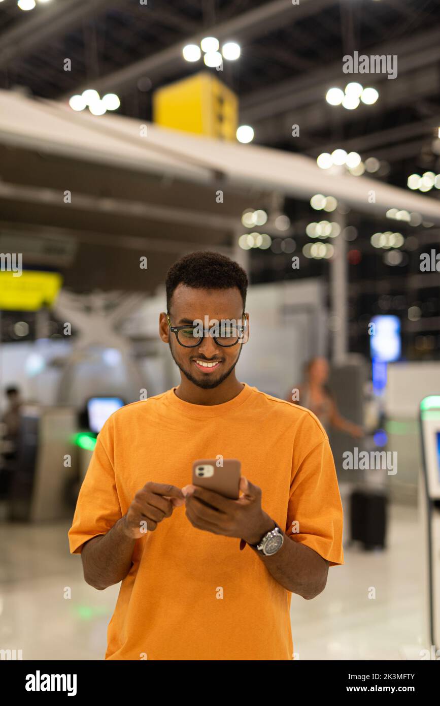 Young handsome black man ready to travel at airport terminal waiting for flight while using phone Stock Photo