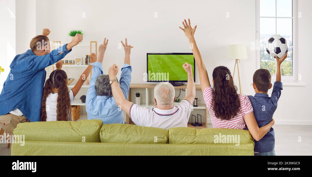 Excited big family sitting on sofa at home together watching football match on TV. Stock Photo
