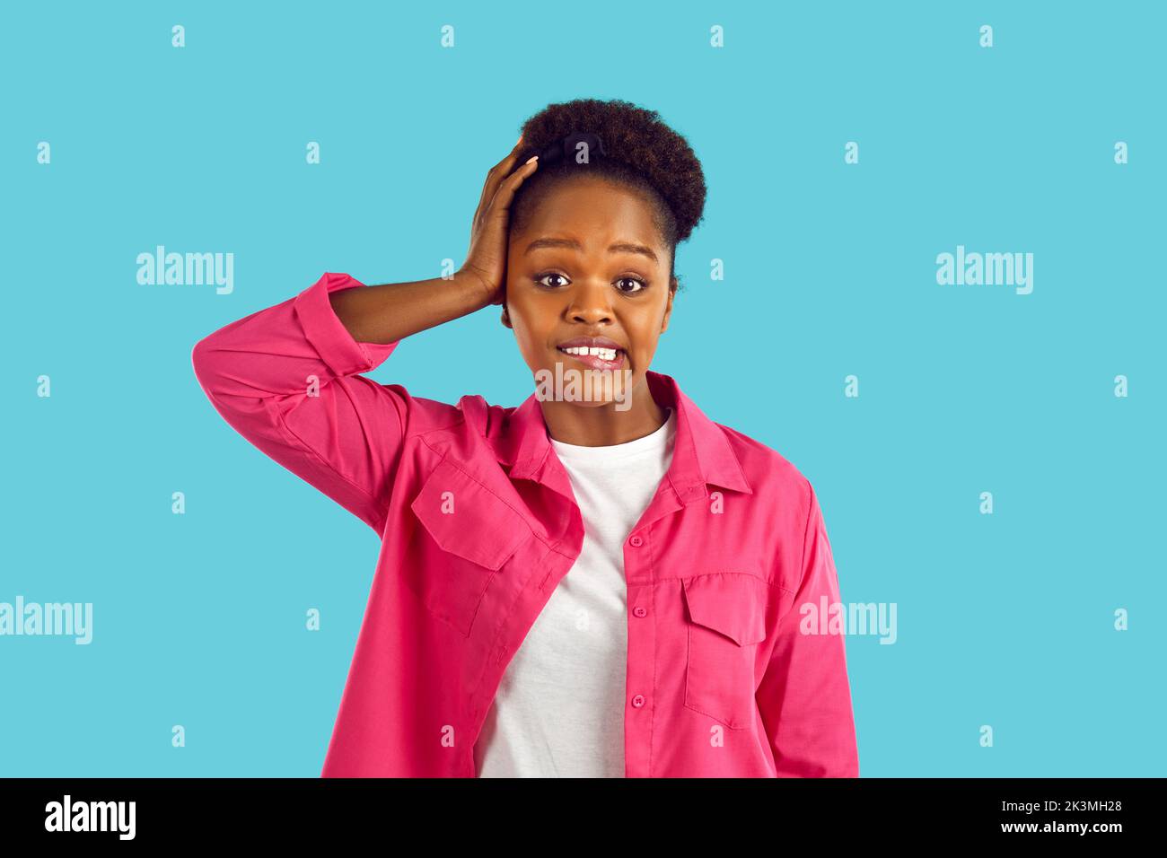 Confused puzzled african american young woman in pink jacket on blue background. Stock Photo