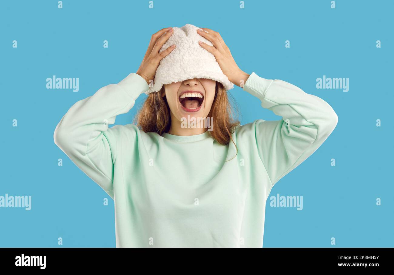 Funny happy young woman laughs as she covers her eyes with bucket hat on her head Stock Photo