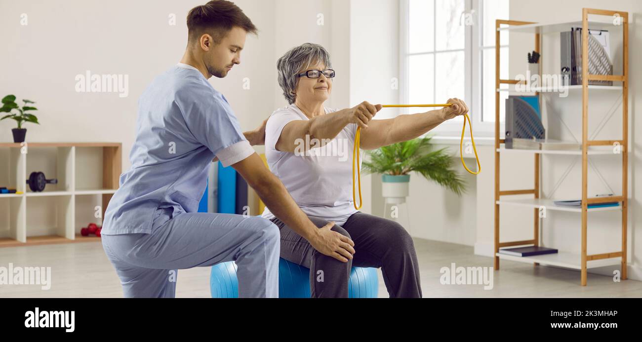 Physiotherapist helping senior woman with osteoporosis do rehabilitation exercises on fit ball Stock Photo