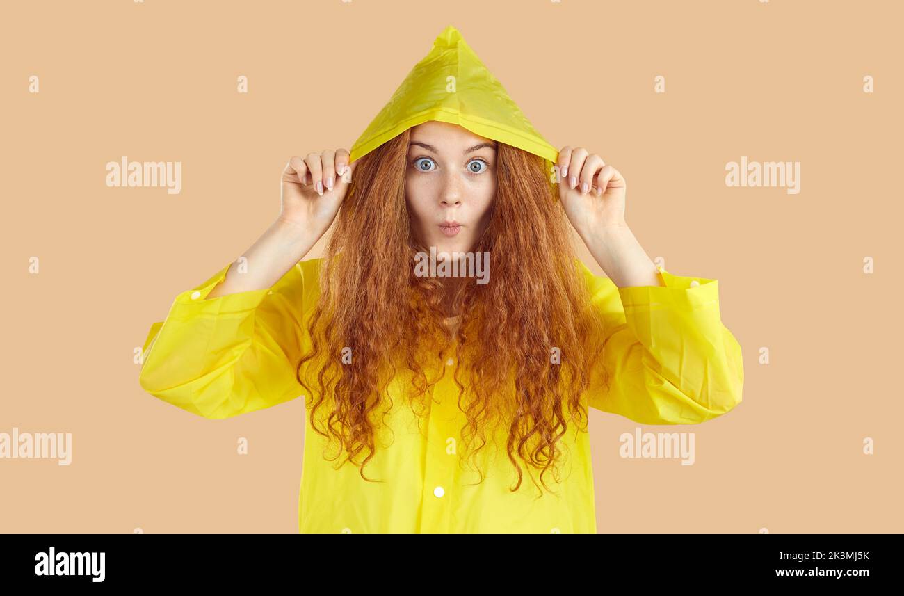 Cheerful emotional young woman in raincoat looking at camera with funny expression. Stock Photo