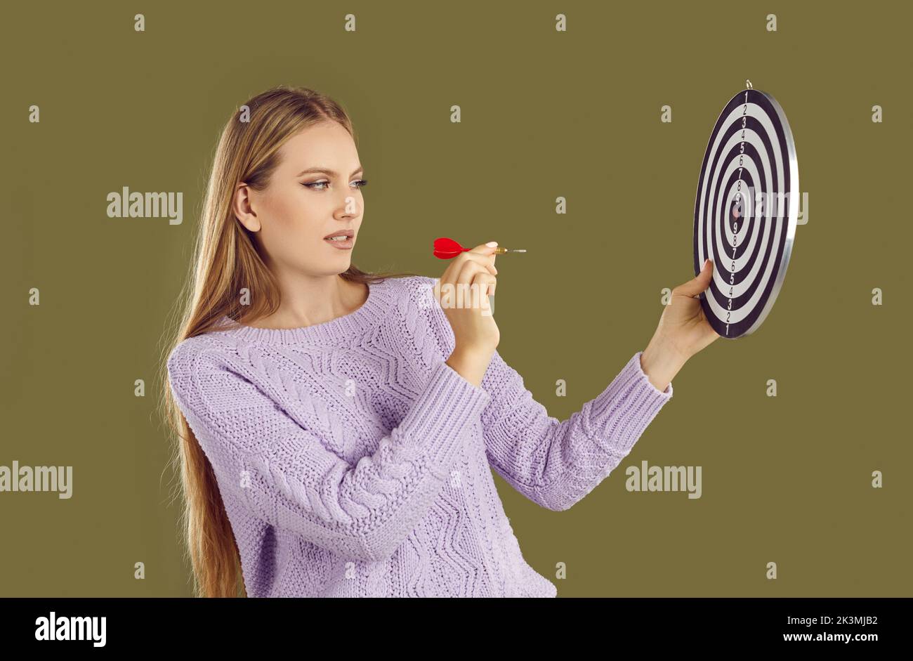 Serious young woman sets a business goal and aims a dart arrow at a shooting target Stock Photo