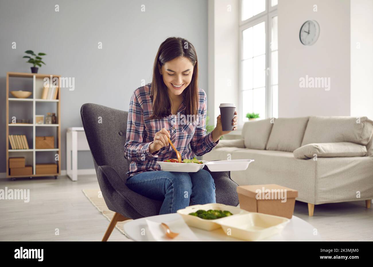 Happy woman drinking coffee and eating vegetable salad from takeout meal delivery Stock Photo
