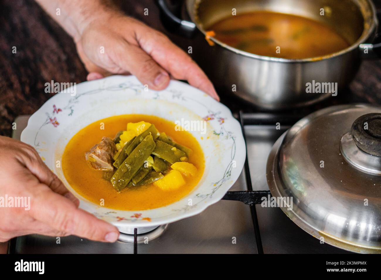The high-angle view of hands holding a bowl of homemade stew over the stove Stock Photo
