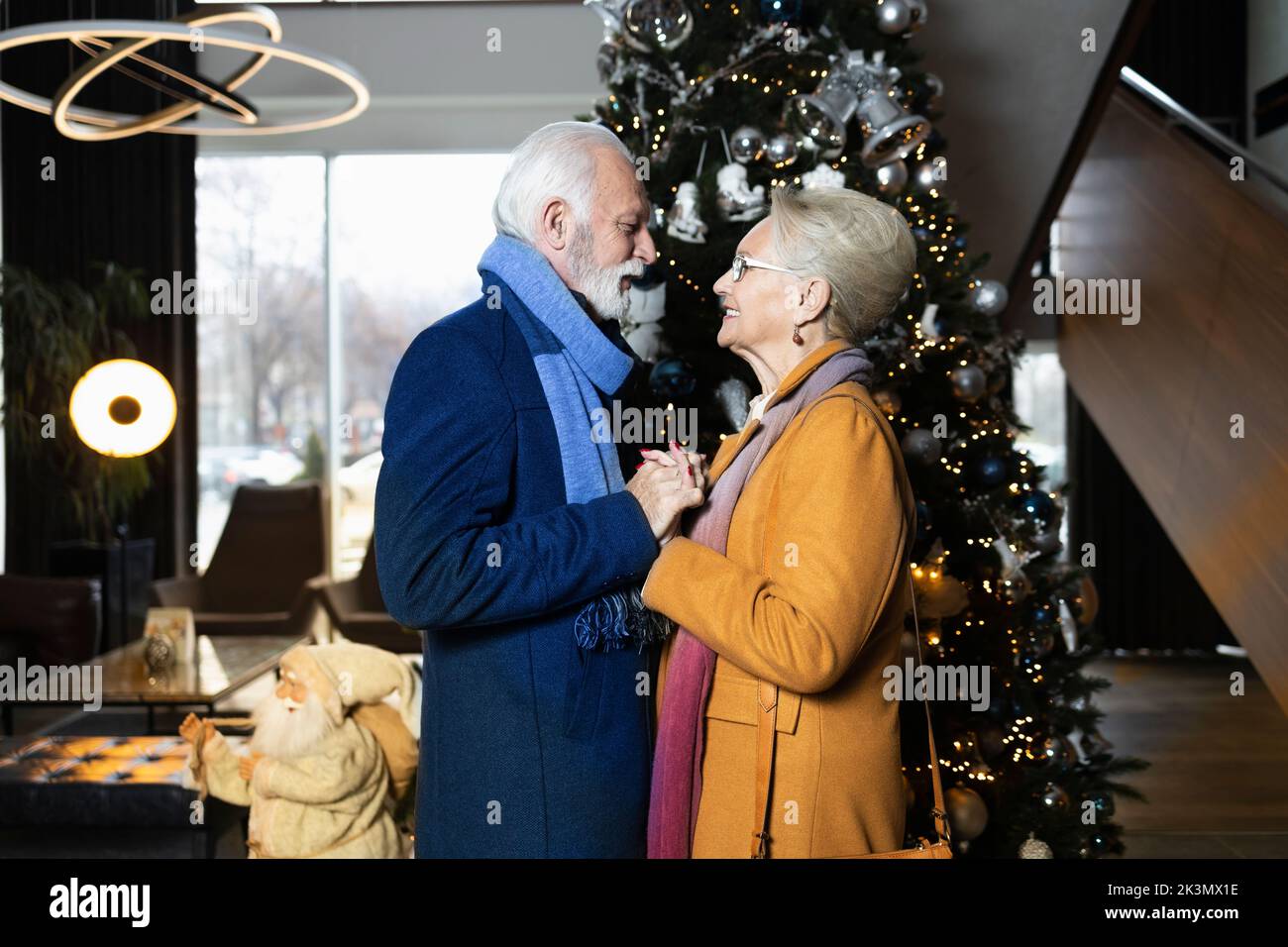 Two elderly people holding hands by the Christmas tree Stock Photo