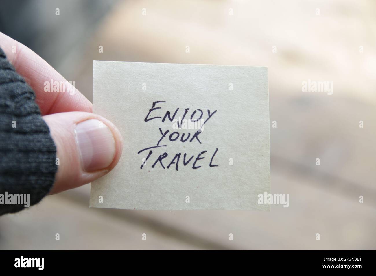 A hand holds a tag with the inscription Enjoy your travel. Stock Photo