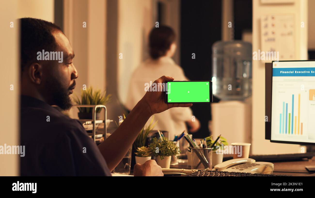 African american man using smartphone with greenscreen, looking at mobile phone with blank copyspace template at sunset. Working with isolated mockup screen and chroma key display. Stock Photo