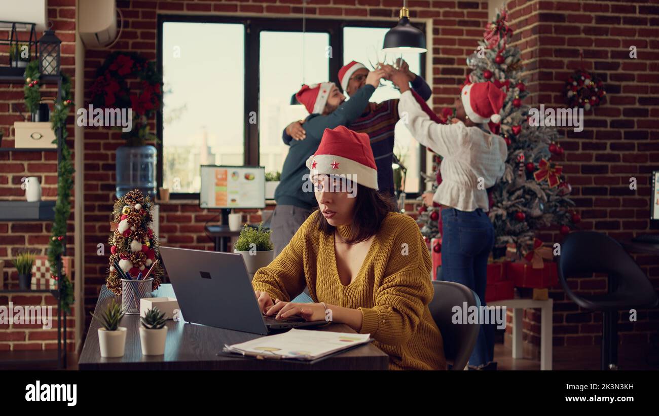 Stressed woman being disturbed by festive noise and colleagues celebrating christmas eve. Feeling frustrated and tired, interrupting work because of noisy people, xmas winter holiday season. Stock Photo