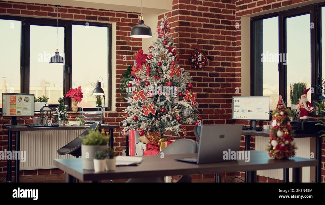 Christmas tree and decorations in company office, festive ornaments and lights to celebrate xmas winter holiday. Empty workplace with seasonal decor for celebration, santa tradition. Stock Photo