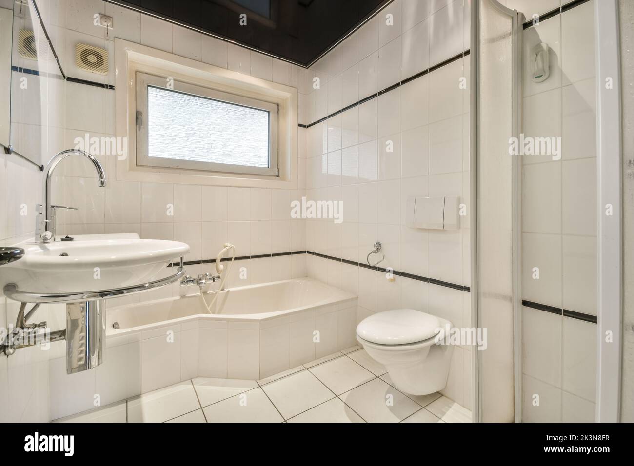 Flush toilet located between sink and shower in small tiled bathroom of