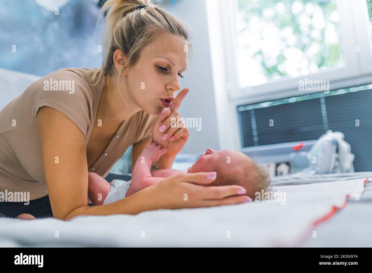 Couple months old baby boy screaming and crying during a diaper change. His mom showing a shhh sign and trying to calm her son down. High quality photo Stock Photo
