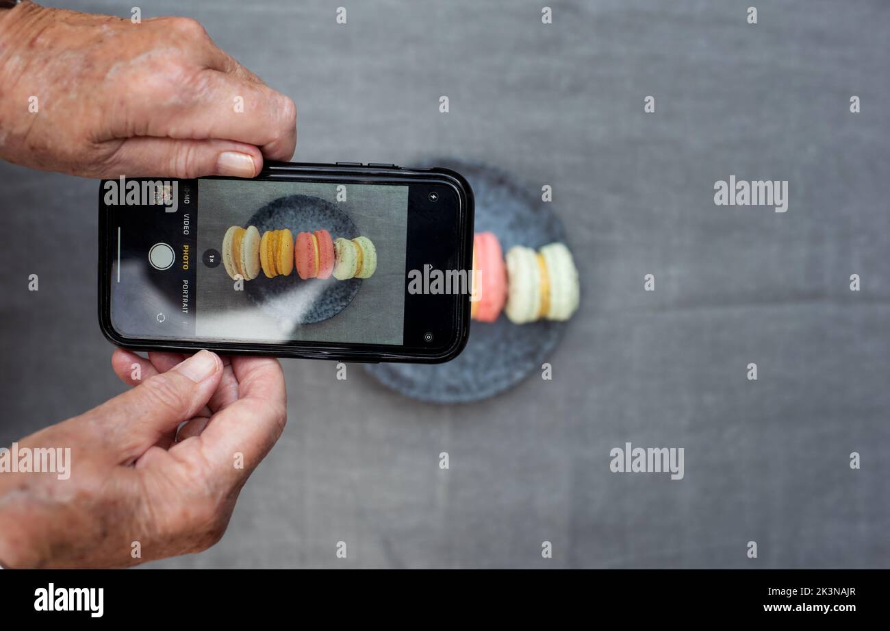 retired woman taking pictures of her macarons on her phone Stock Photo